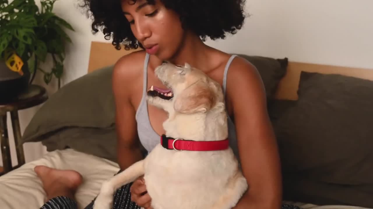 A woman holding and kissing her happy dog on a bed